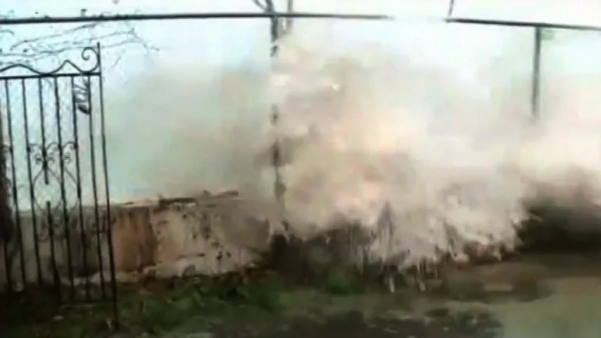 A wave breaking over a low wall and fence during the storm.