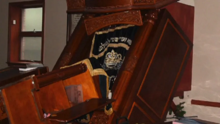 A toppled aron kodesh with its curtain still attached, in a damaged room.